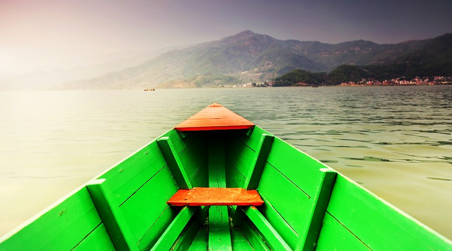Wooden green boat floating on the Fewa Tal lake with view to Pokhara hills in Nepal