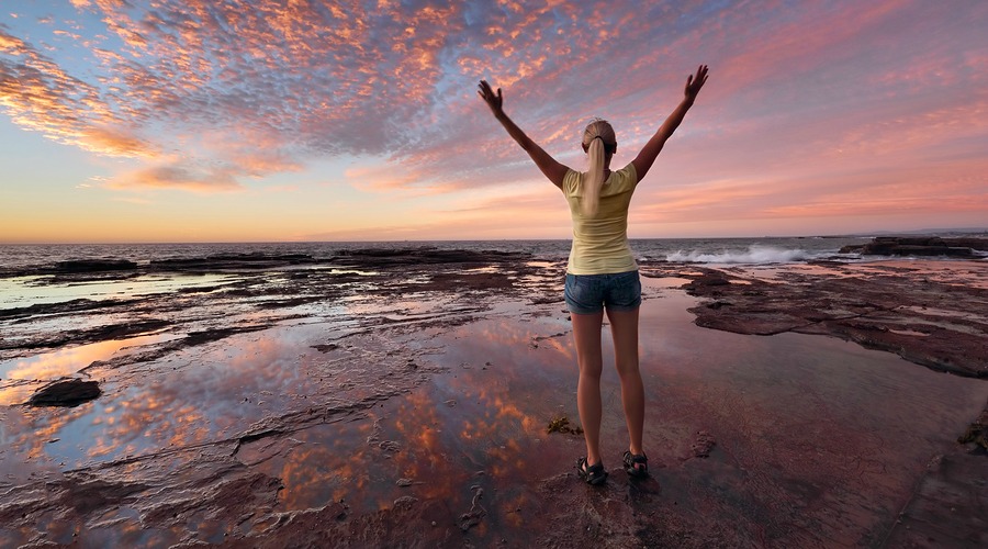 Woman with arms outstretched towards the sunrise sky celebrating life. Jubilation triumph success spiritual exhilaration