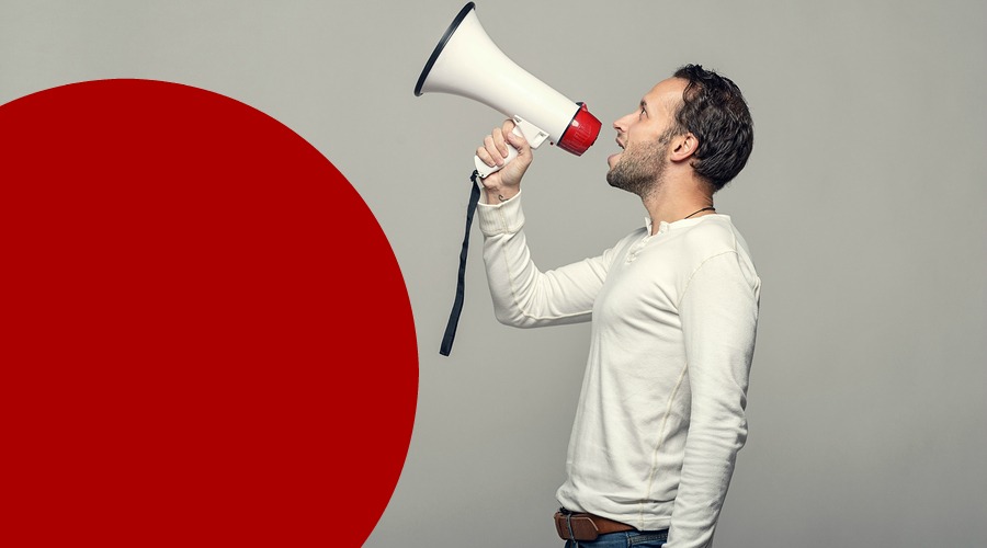 Man speaking over a megaphone as he makes a public address participates in a protest or organises a rally or promotion over grey with copy space to the side