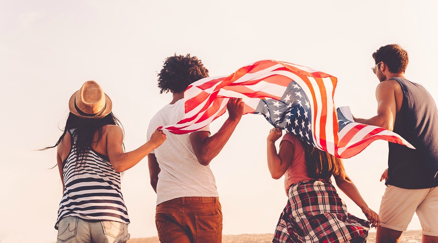 Friends with American flag. Rear view of four young people carrying american flag while running outdoors